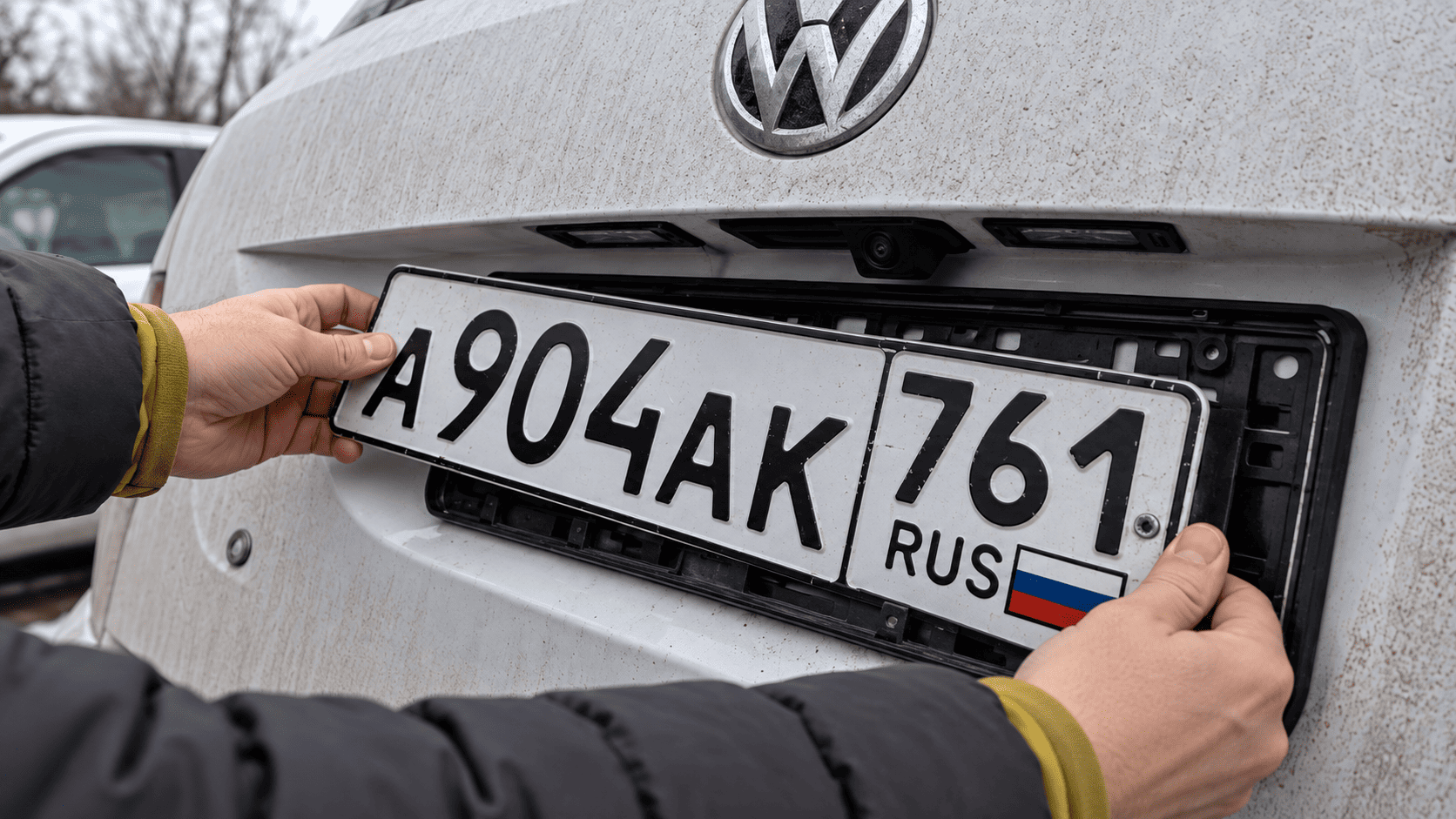 Автомобилист аккуратно извлекает государственный номер из держателя двумя руками